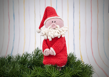 Gehäkelter Weihnachtsmann in rotem Mantel mit weißem Bart auf Tannenzweigen