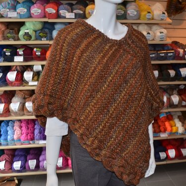 Braun-melierter Strickponcho mit gezopftem Saum auf Schaufensterpuppe vor Wollregal