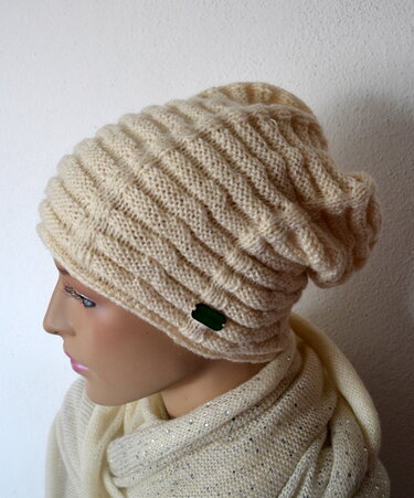 Beige gestrickte Slouch-Beanie mit Rippenmuster auf Schaufensterkopf, seitliches grünes Label
