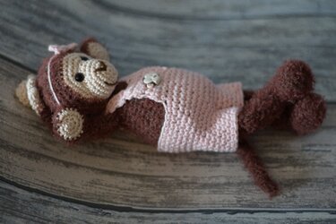 Gehäkelter brauner Amigurumi-Affe mit rosa Kleid liegend auf Holzuntergrund