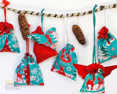 Verschiedene genähte Stoffsäckchen mit Kordelzug und weihnachtlichen Motiven, an einem Ast aufgehängt