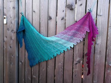 Farbintensives gestricktes Tuch mit welligem Rand und Farbverlauf, aufgehängt an einer Holzvertäfelung