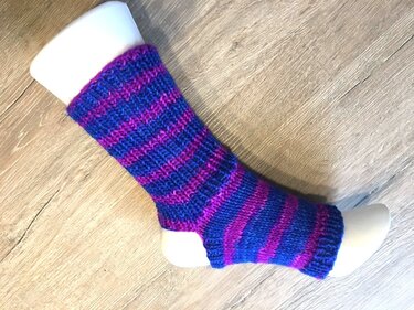 Gestrickte Fußstulpe mit blauen und violetten Streifen auf weißem Fußmodell