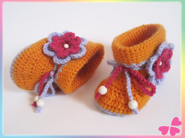 Paar gehäkelter Babyschuhe orange mit lila-pinker Blüte und weißen Perlen