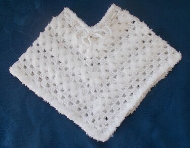 Weißer gehäkelter Babyponcho mit Schleife auf blauem Hintergrund
