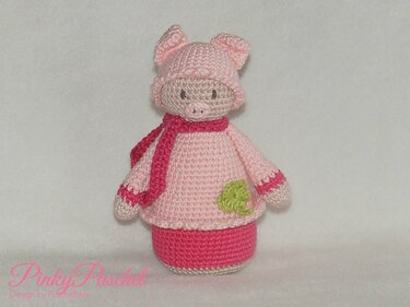 Rosa gehäkeltes Amigurumi‑Schweinchen mit Mütze, Schal und grünem Kleeblatt