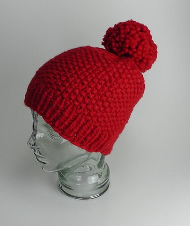 Rote gestrickte Mütze mit Bommel auf einem gläsernen Schaufensterkopf