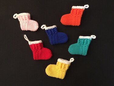 Sechs bunte gehäkelte Mini-Stiefel mit weißem Bündchen auf dunklem Hintergrund