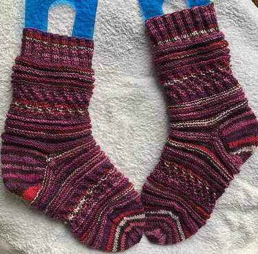 Handgestrickte Socken in Violett- und Rottönen auf weißer Unterlage