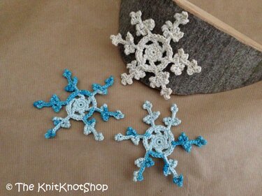 Drei gehäkelte Schneeflocken in Blau und Creme auf hellem Untergrund