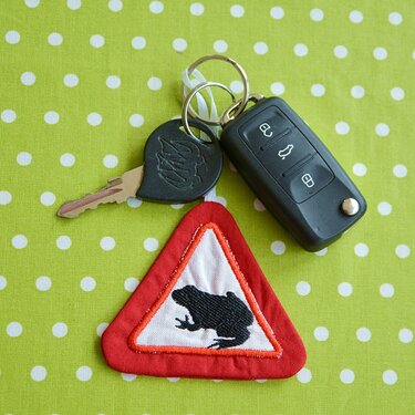 Roter, dreieckiger ITH-Stick-Schlüsselanhänger mit weißem Feld und schwarzer Frosch-Silhouette am Schlüsselbund