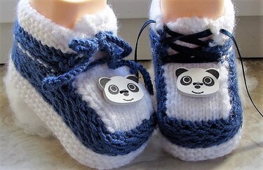 Paar gestrickter blau-weißer Babyschuhe mit Panda-Applikation und Schnürung