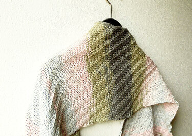 Gestricktes Rechtecktuch mit diagonaler Rippenstruktur und Farbverlauf, aufgehängt an einem Bügel