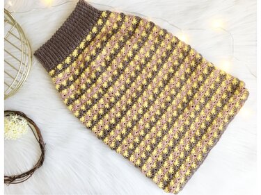 Flach gelegter gehäkelter Babysack mit elastischem Rippenbündchen und gelb-rosa Streifen auf braunem Grund