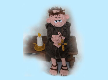 Amigurumi monk doll in brown habit holding a cross beside a crochet candle on a wooden bench