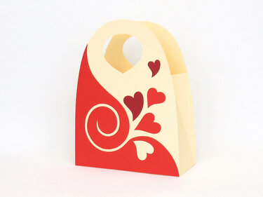 Creme-rote Geschenkverpackung aus Papier mit Herzmotiven und geschwungenem Muster, mit Griff oben.