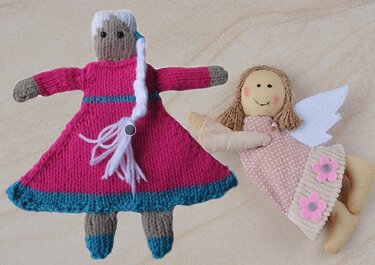 Gestrickte Babypuppe mit rosa Kleid und geflochtenem weißem Zopf neben einem Stoffengel mit Flügeln