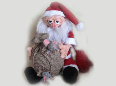 Seated crocheted Santa Claus doll in a red suit and long hat holding a brown sack with two small gray mice.