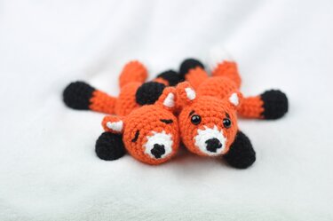 Zwei kleine gehäkelte Füchse in Orange, Schwarz und Weiß nebeneinander auf weißer Oberfläche