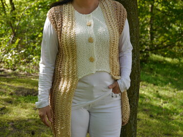 Lange gestrickte Damenweste in Beige und Creme mit drei Holzknöpfen, getragen über weißem Langarmshirt.
