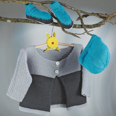 Gestrickte graue Kinderjacke an Holzbügel, daneben türkisfarbene Mütze und Hausschuhe