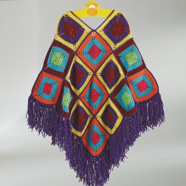 Bunter gehäkelter Poncho aus Granny‑Squares mit violetten Fransen an gelbem Bügel