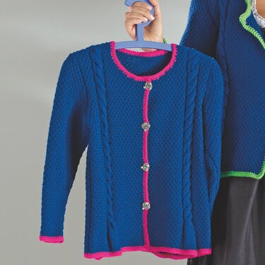 Blaue gestrickte Kinderjacke mit pinken Kanten, Zopfmuster und dekorativen Knöpfen an einem Kleiderbügel