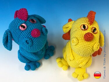 Zwei gehäkelte Amigurumi-Drachen, einer blau mit pinken Akzenten, einer gelb mit orangefarbenen Akzenten