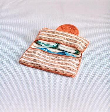 Gehäkeltes Windeltäschchen in Beige, Weiß und Orange mit eingesteckten Windeln und Feuchttüchern auf einer hellblau gemusterten Decke