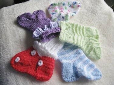 Fünf Paar handgestrickte Babysocken in Lila, Weiß mit buntem Muster, Hellgrün, Hellblau gestreift und Rot mit Verzierungen auf weißem Fleece