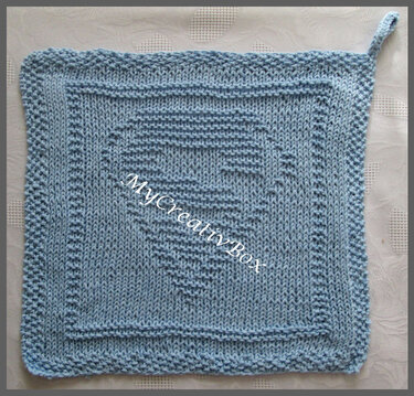 Quadratischer hellblauer Topflappen mit kraus gestricktem Rand und erhabenem Herz-Relief