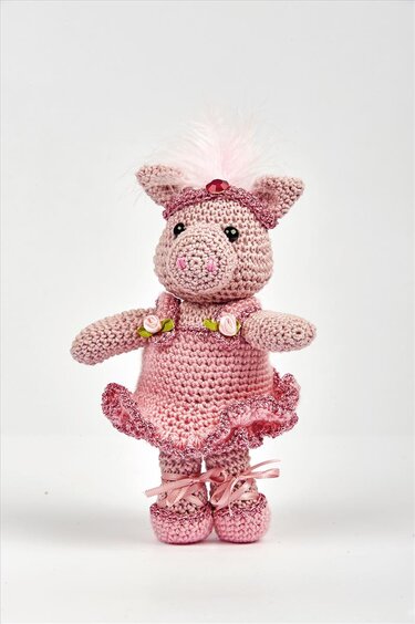 Rosa gehäkeltes Amigurumi-Schwein mit Rüschentutu, Federkopfschmuck und geschnürten Schuhen vor hellem Hintergrund