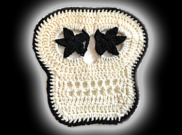 Gehäkelte Totenkopf-Applikation weiß mit schwarzem Rand und blütenförmigen schwarzen Augen