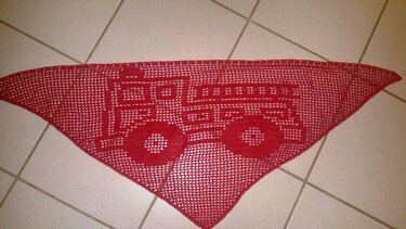Rotes, dreieckiges, gehäkeltes Tuch mit Feuerwehrauto‑Motiv auf hellem Fliesenboden.