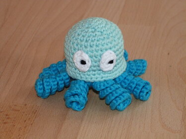 Gehäkelter Oktopus hellblau-türkis mit großen Augen auf Holzboden