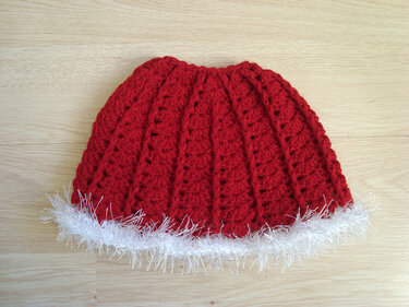 Red crocheted ribbed beanie with white fluffy trim on wooden background