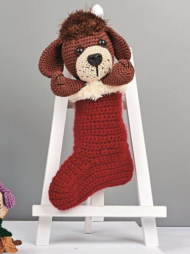 Gehäkeltes Amigurumi: brauner Hund schaut aus rotem Weihnachtsstiefel mit weißem Rand