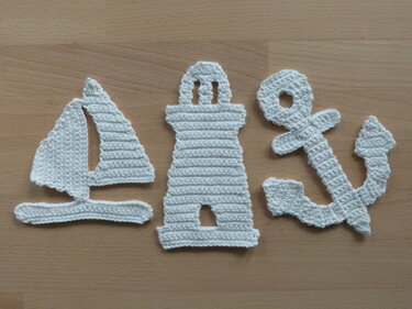Weiße gehäkelte Applikationen: Segelboot, Leuchtturm und Anker auf Holzuntergrund