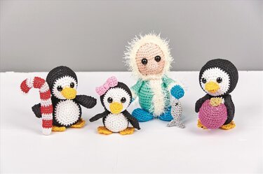 Vier gehäkelte Amigurumi-Figuren: drei Pinguine mit Accessoires und eine Puppe mit flauschiger Kapuze