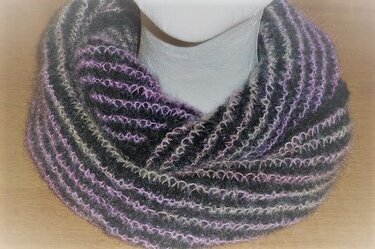Gestrickter Loop-Schal auf Schaufensterpuppe mit schwarzen und lilafarbenen Rippenreihen