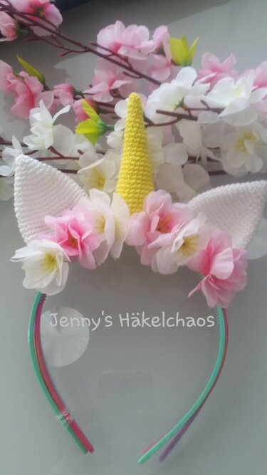 Gehäkeltes Einhorn-Stirnband mit gelbem Horn, weißen Ohren und rosa Blüten auf mehrfarbigem Haarreif
