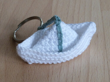 Gehäkelter weißer Boot-Schlüsselanhänger mit grünem Band an Metallring auf Holzoberfläche