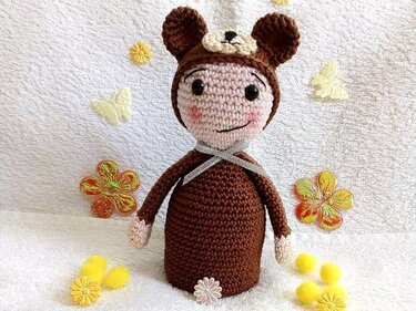 Gehäkelte Amigurumi-Puppe in braunem Bärenkostüm mit Schleife und rosigen Wangen
