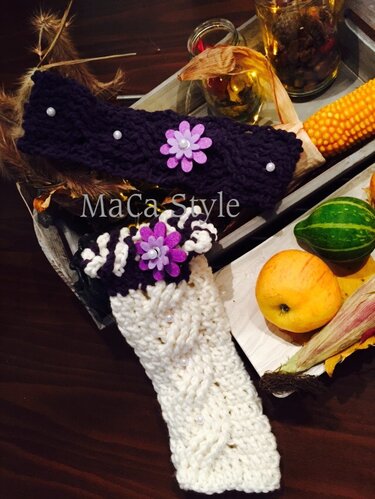 Dunkellila gehäkeltes Stirnband mit Perlen und lila Filzblüte und weiße gehäkelte Stulpe mit strukturierter Musterung, auf Holztisch mit herbstlicher Dekoration