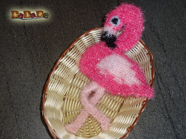 Rosa flauschiger gehäkelter Flamingo in kleinem Korb auf dunklem Untergrund