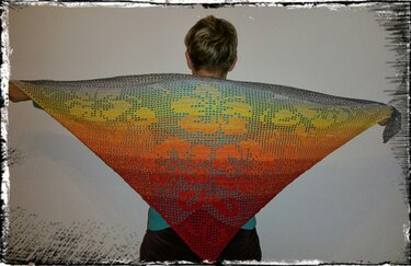 Rückenansicht einer Person, die ein dreieckiges gehäkeltes Tuch mit Blumenmotiv und Farbverlauf hält