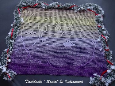Gehäkelte Filet-Tischdecke mit 'Merry Christmas' und Santa-Motiv, Ombre-Farbverlauf Lila-Gelb, umrandet von einer glitzernden Girlande und roten Bändern