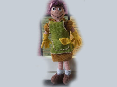 Crocheted amigurumi doll with purple hair, green apron, brown skirt, yellow gloves, and brown shoes