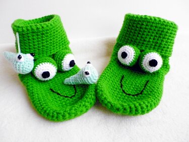 Grüne, handgehäkelte Hausschuhe mit weißen Augen und gesticktem schwarzen Lächeln