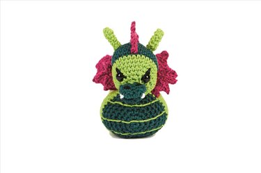 Grün-pinker gehäkelter Amigurumi-Drache mit gestreiftem Körper, pinkem Kamm und seitlichen Zacken